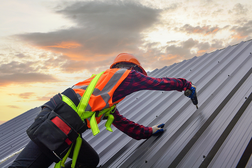 Roofing installer screwing in a metal panel.